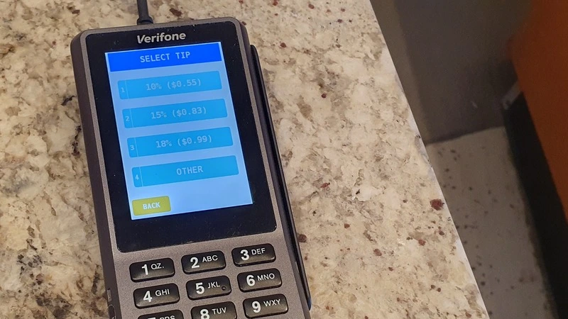 Photograph of a card payment terminal showing three percentage tipping options (10, 15, 18%), an 'other' option, but no option not to tip